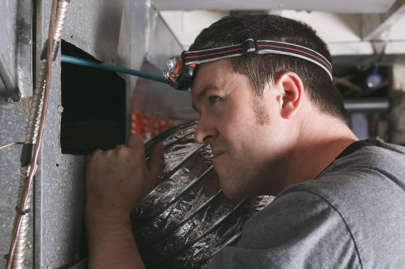 Why Is My Furnace Leaking Water? Photo of a technician performing maintenance on a furnace.