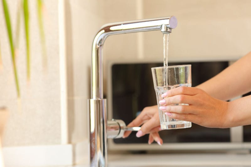 Woman using a glass to get water from the sink faucet. What is Reverse Osmosis and how does it work?