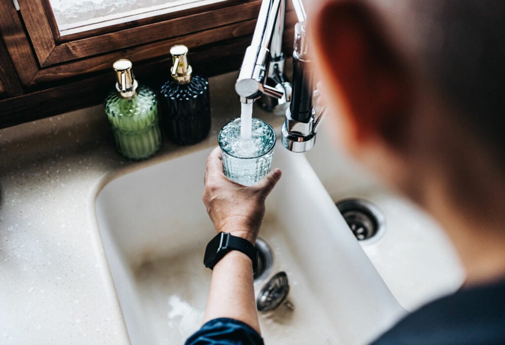 A man getting running clean drinking water from his sink into a clear glass cup.