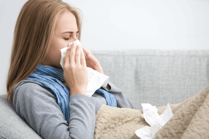 woman on couch blowing nose.